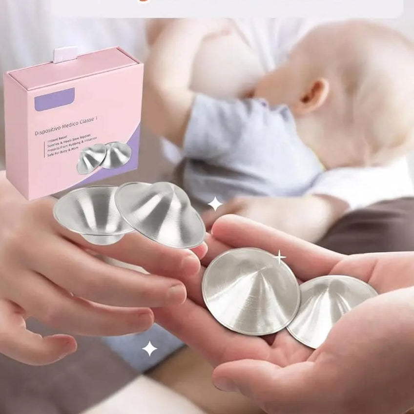 Silver breast pads held by hands with a baby in the background and a pink packaging box.