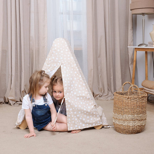 Two children playing inside a polka dot tent in a room with curtains and a basket.
